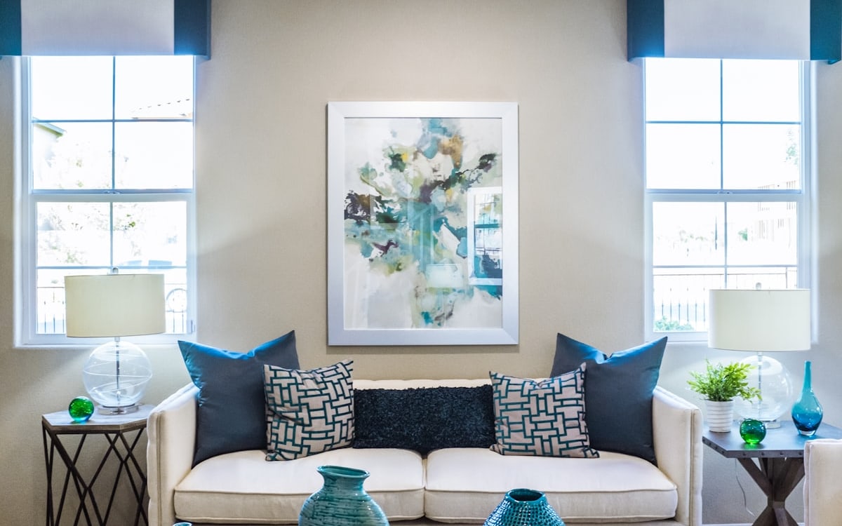 Sala decorada com sofá branco, almofadas estampadas e quadro na parede